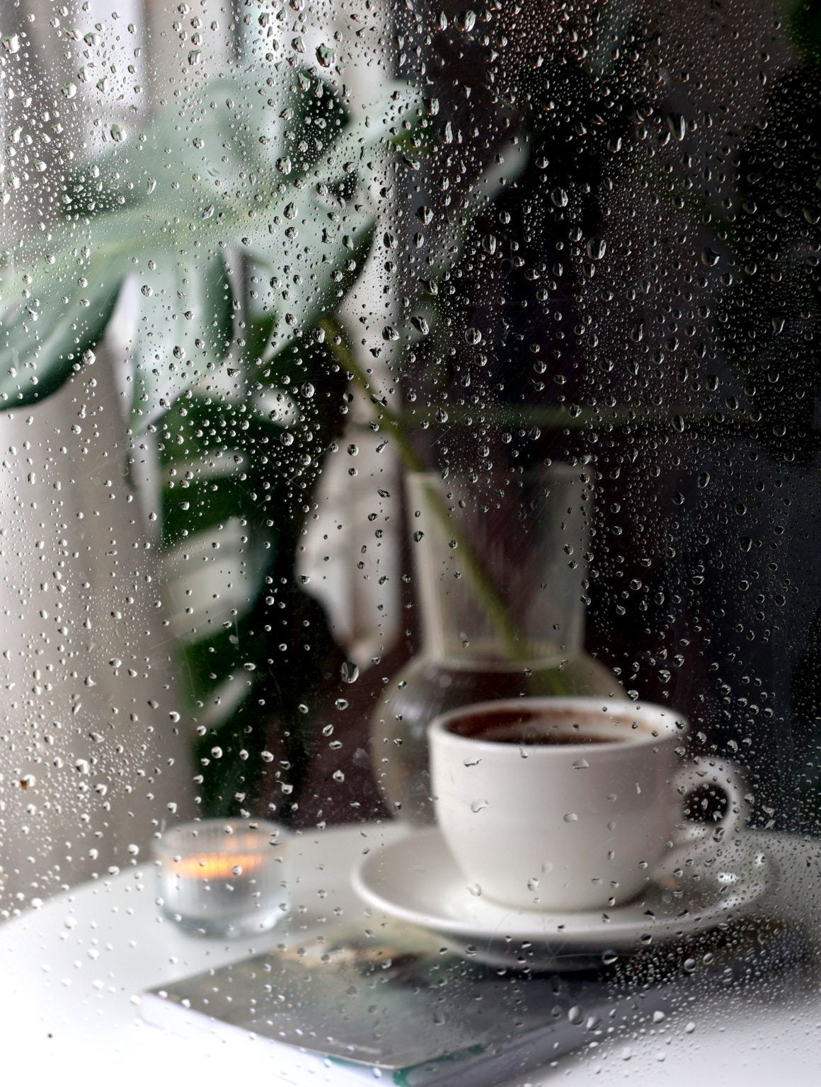 Coffee cup on a windowsill against rain-blurred glass